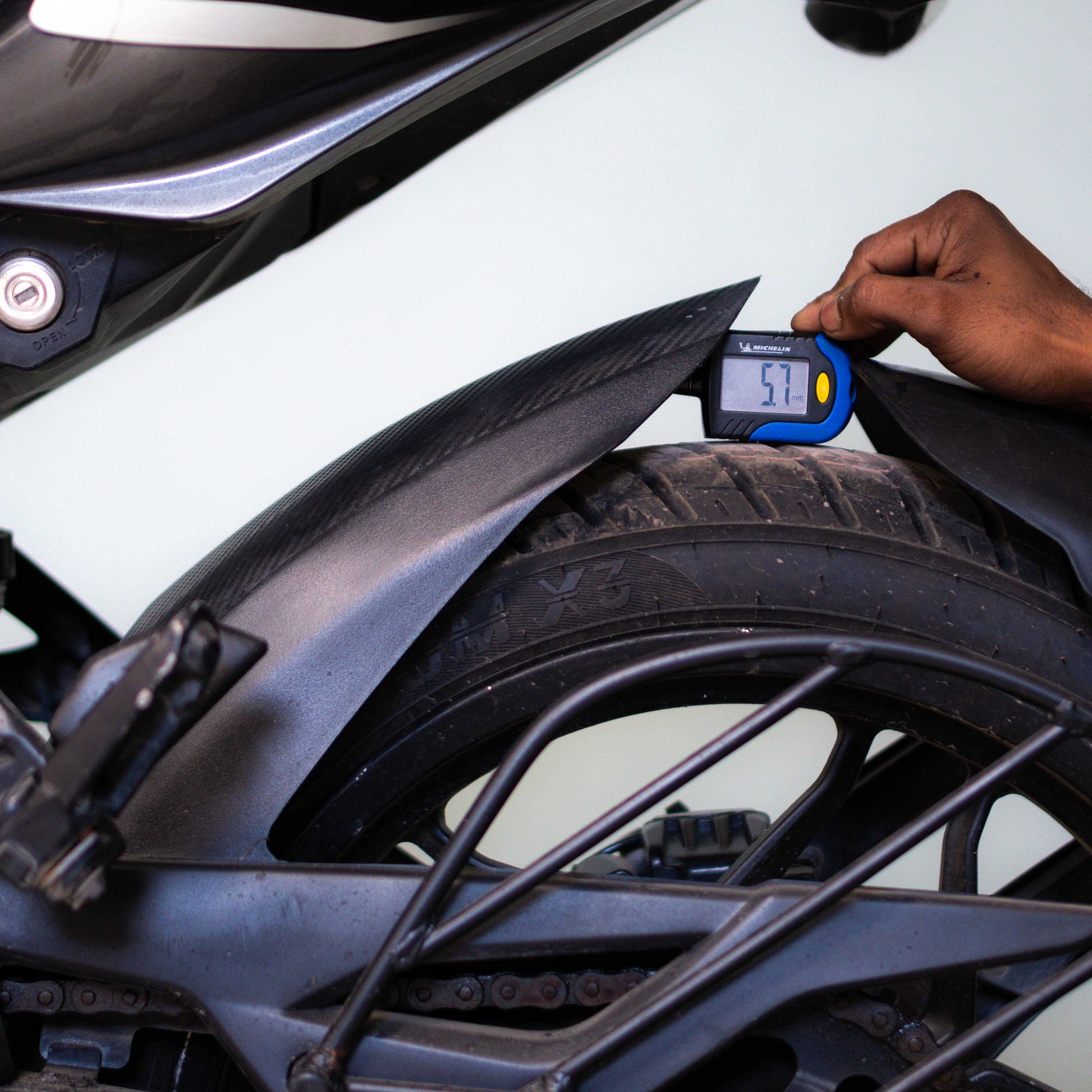 Hand using a digital tire pressure gauge on a motorcycle tire