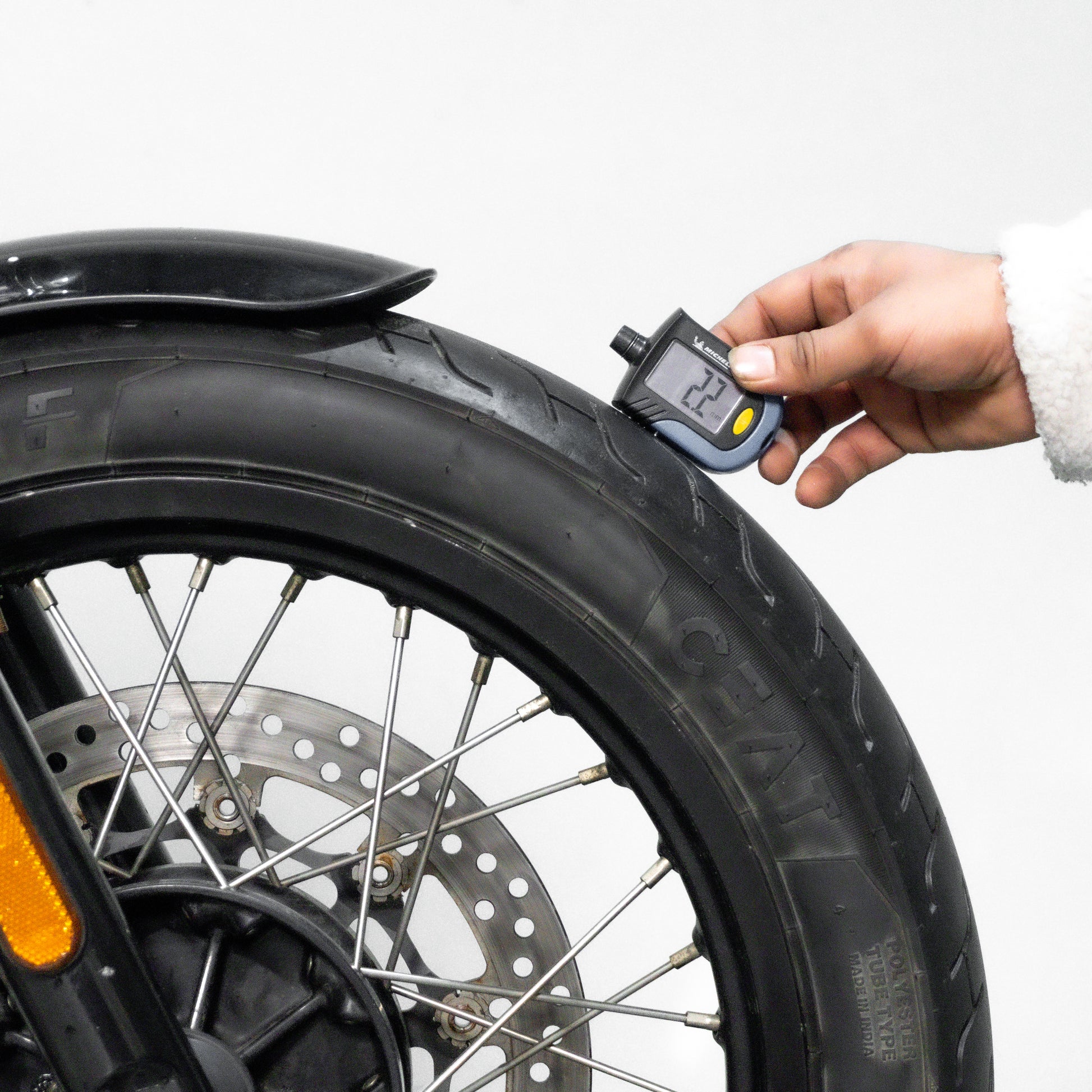 Hand using a digital tire pressure gauge on a motorcycle tire against a white background