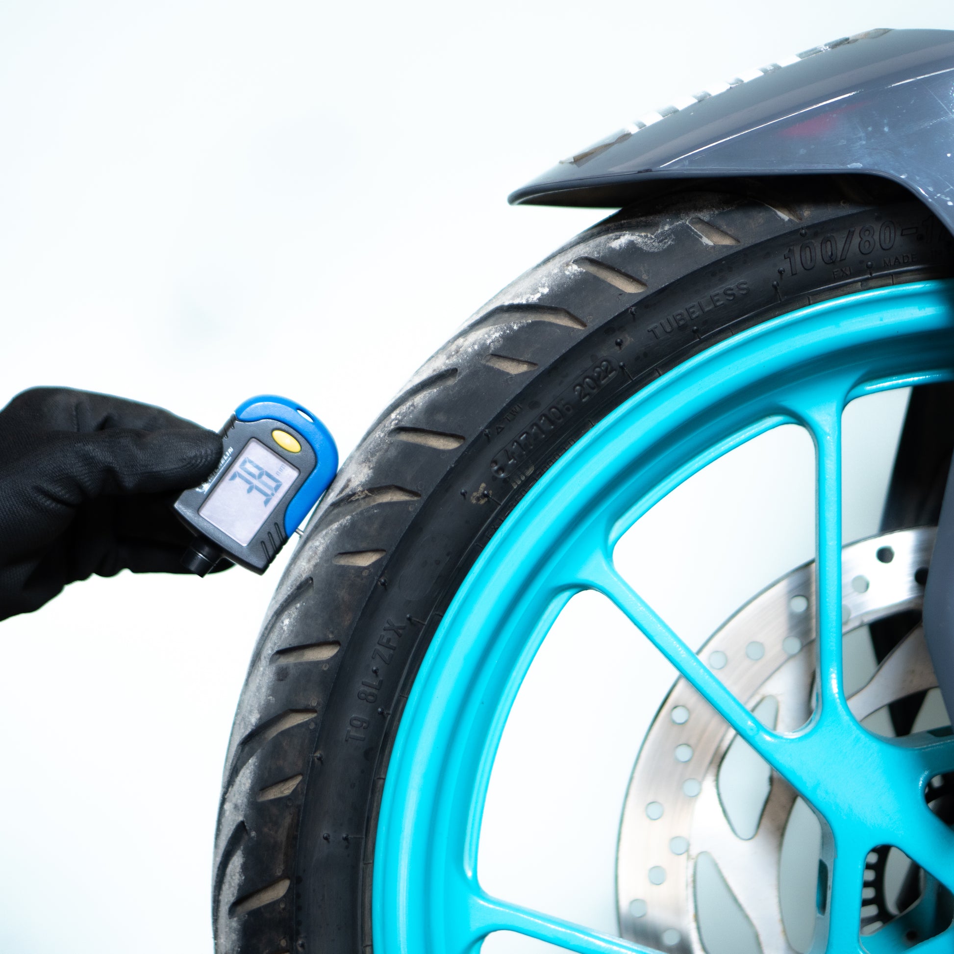 Person using a digital tire pressure gauge on a motorcycle tire.